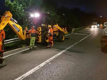 Nighttime road construction with workers and machinery under streetlights.