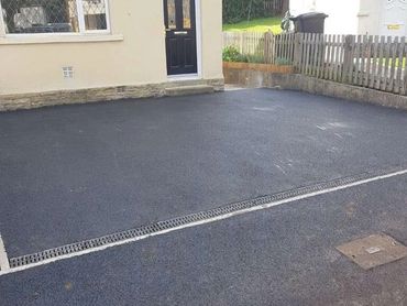 Newly paved driveway outside a house with a black door and window.