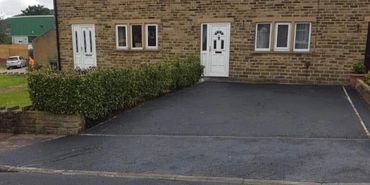 A brick house with two white doors and a freshly paved driveway.