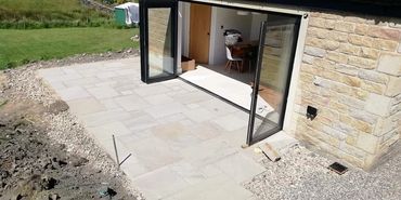 Stone patio outside a house with open glass doors leading to an interior dining area.