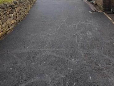 A newly paved road with chalk drawings and two people standing near a garage.