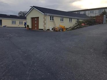 A newly paved driveway leading to a beige house with construction materials nearby.