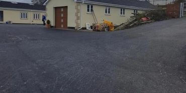 A newly paved driveway leading to a beige house with construction materials nearby.
