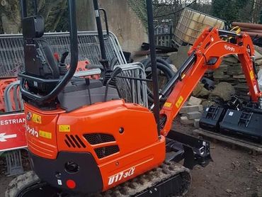 Orange Kubota U17-3α mini excavator on dirt ground with construction materials in the background.