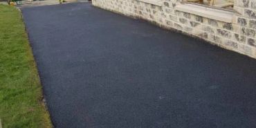 Freshly paved black asphalt pathway along a stone wall with picnic tables.