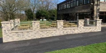 Stone wall with glass panels and rope fencing outside a building on a sunny day.