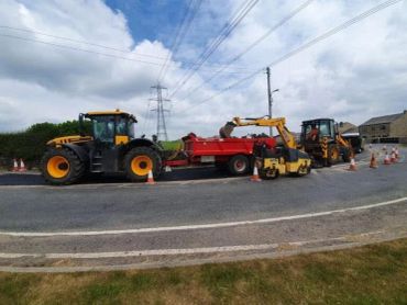 Construction vehicles and cones on a rural road under a partly cloudy sky.