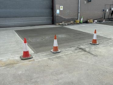 Freshly poured concrete section cordoned off by traffic cones outside a warehouse.