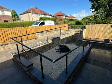 Modern garden patio with black railings and stone seating under a blue sky.