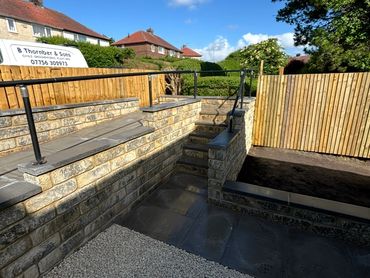 Newly constructed stone steps and retaining walls with metal railings in a residential garden.