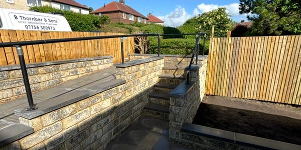 Stone terraced garden steps with metal railing under clear blue sky.