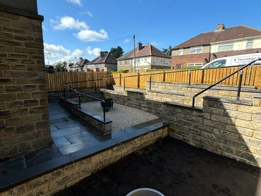 A neatly landscaped backyard with stone walls, a gravel area, and a flowerpot in the foreground.