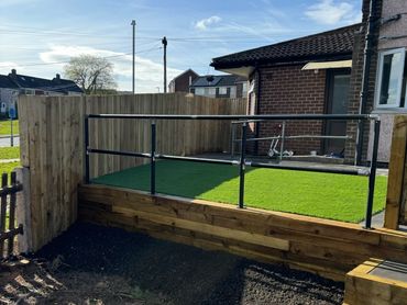 A small fenced backyard with artificial grass and wooden steps.