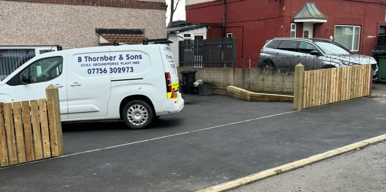 A white van and a silver car parked in driveways with new wooden fences.