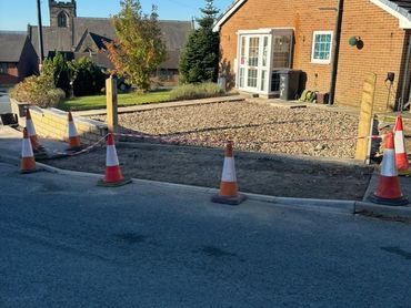 Construction cones and tape mark a driveway under renovation beside a brick house.