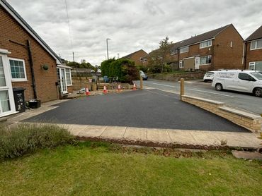 Newly paved driveway in a suburban neighborhood under a cloudy sky.