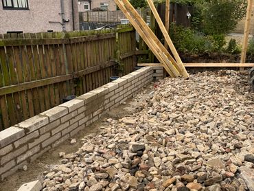 Construction site with bricks, gravel, and wooden planks near residential houses.