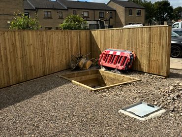 A fenced backyard with gravel and an open wooden pit under construction.
