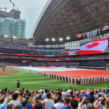 Crowd and military personnel holding a large Canadian flag at a stadium.