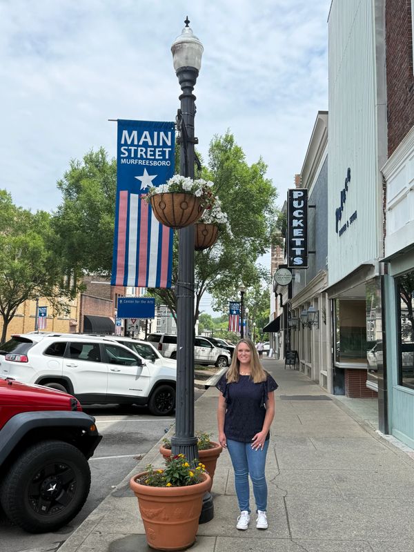 A woman stands on Main Street in Murfreesboro beside a lamppost with hanging flower baskets.