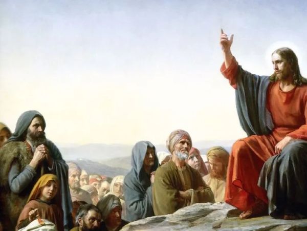 Jesus teaches a crowd, raising his hand in blessing or instruction.