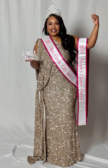 A crowned woman in a sparkling gold gown holds a crown and sash.
