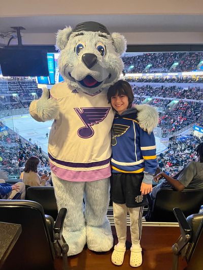 A child poses with a hockey team mascot at an arena.
