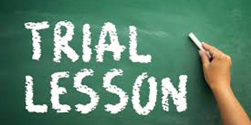 Hand writing 'TRIAL LESSON' on a chalkboard with chalk.