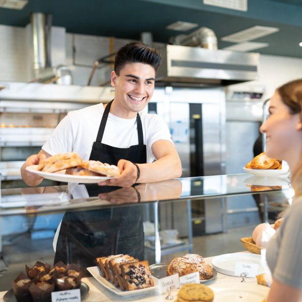 Smiling bakery worker serving pastries to a customer at the counter.