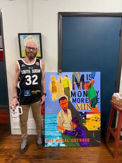 Man standing next to a colorful, socially themed painting indoors.