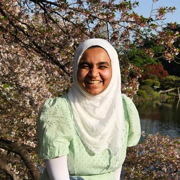 Smiling woman in a white hijab outdoors with blooming trees.