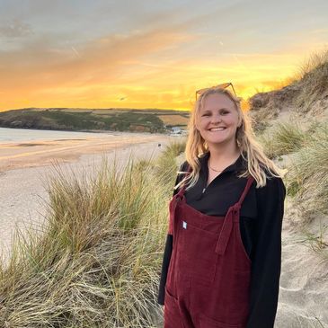Smiling woman in red overalls on a beach at sunset.