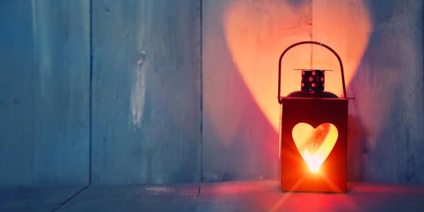 A wood floor and wall, gray with age. A lantern with heart cut-out casts a heart shape onto the wall