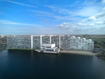 Large modern apartment complex by a calm lakeside under a blue sky.