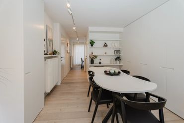 Minimalist dining area with black chairs and white table in a bright room.