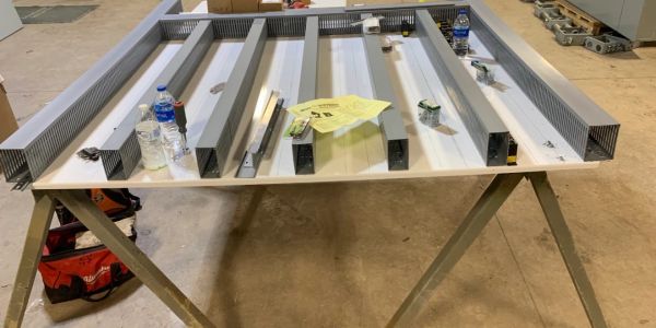 Metal beams and tools arranged on a white table in a workshop.