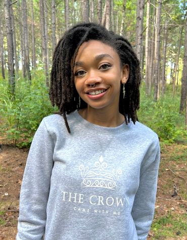 Smiling woman in a grey sweatshirt stands in a forest.