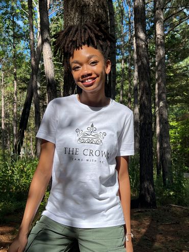 Smiling person in a white t-shirt stands in a sunlit forest.