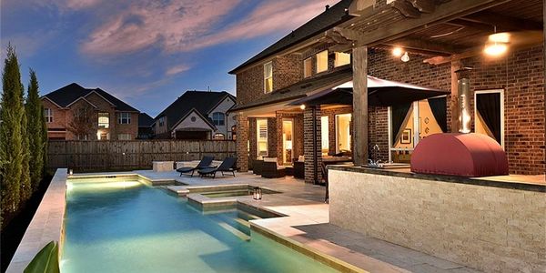 Luxury backyard with illuminated pool and outdoor kitchen at dusk.