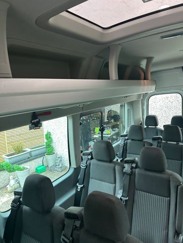Interior view of a passenger van with multiple seats and seatbelts.