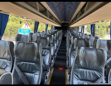 Interior of a clean, empty coach bus with leather seats and seatbelts.