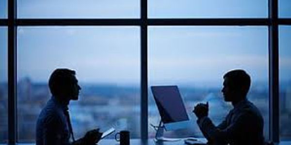 Two professionals discussing work in a modern office with a city view.