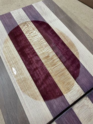 Wooden cutting board with circular and striped patterns in purple and natural tones.