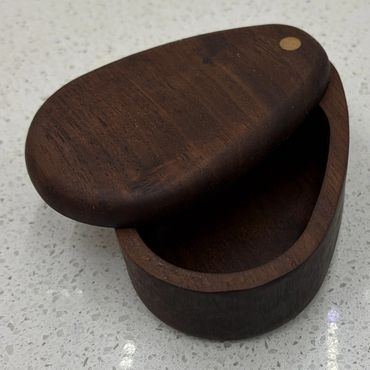 Small oval wooden box with lid on speckled countertop.