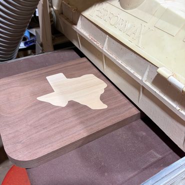 Woodworking machine sanding a wooden piece with Texas state shape.