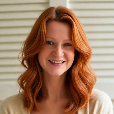 Smiling woman with wavy red hair and a light background.