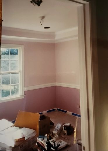 A room under renovation with pink walls and scattered painting supplies.
