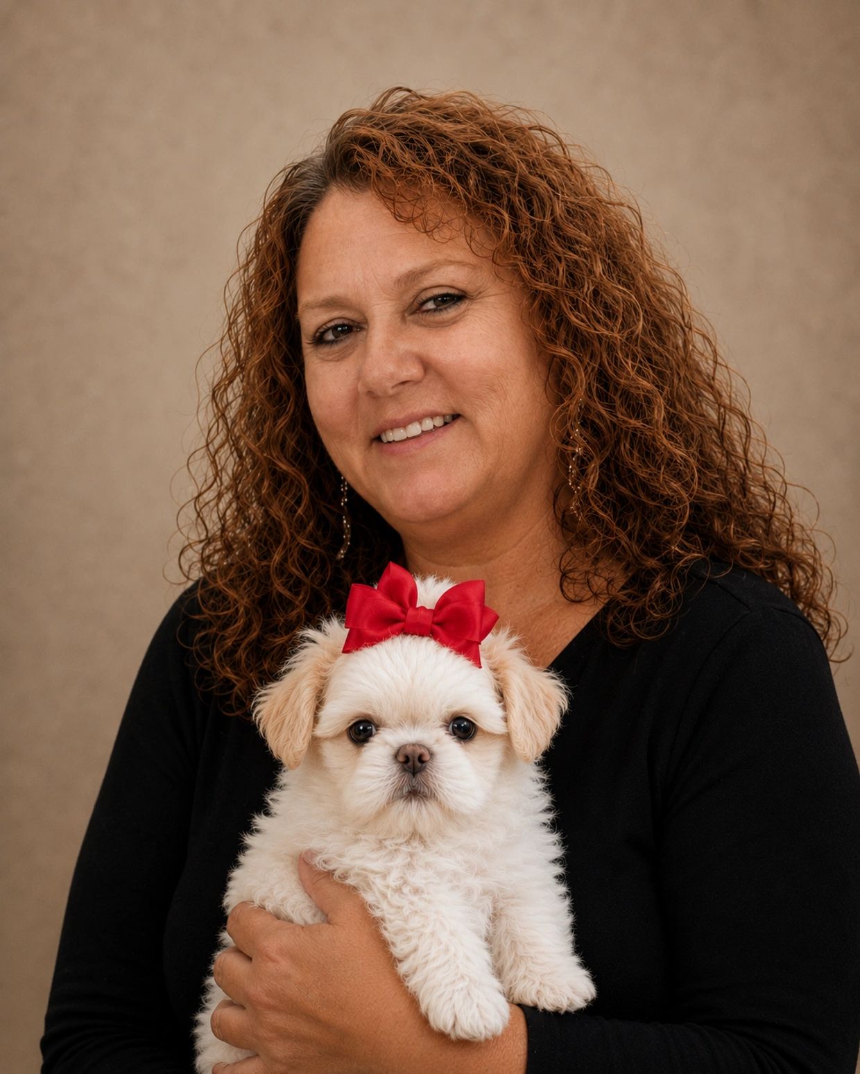 Woman with curly hair holding a small white dog with a red bow.