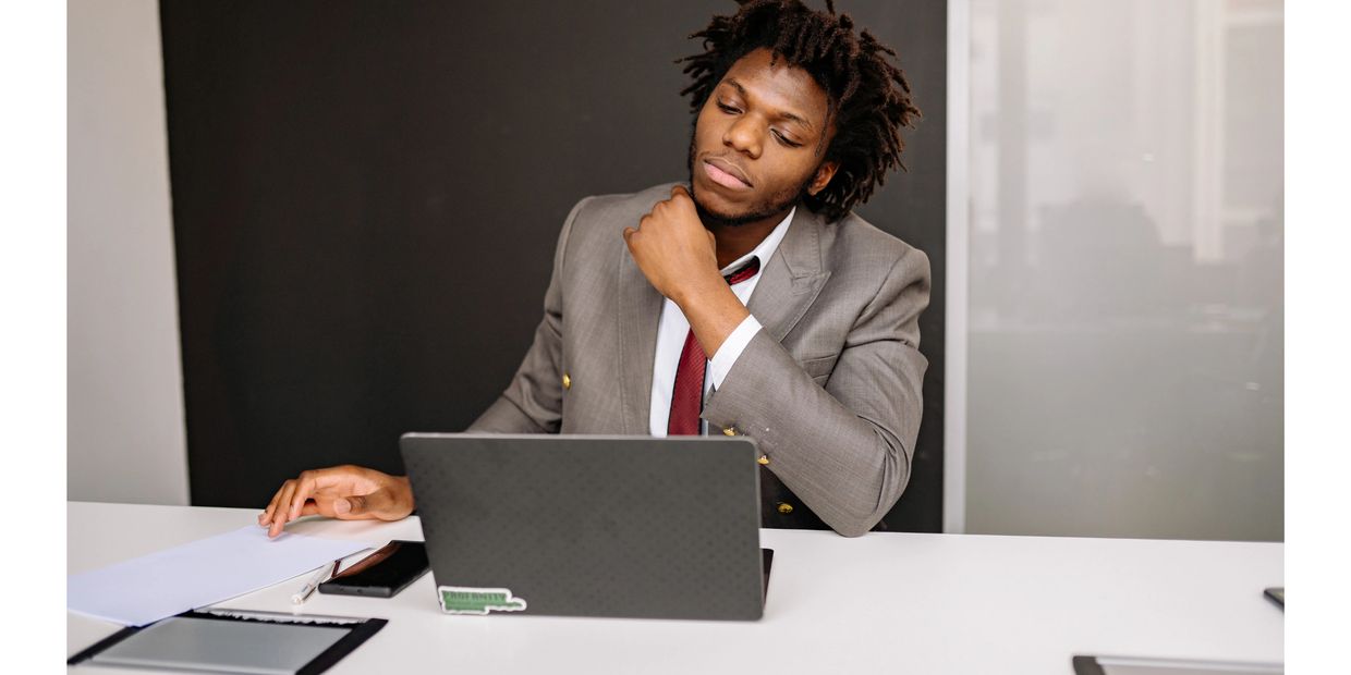 A man in a suit working thoughtfully on a laptop at a desk.