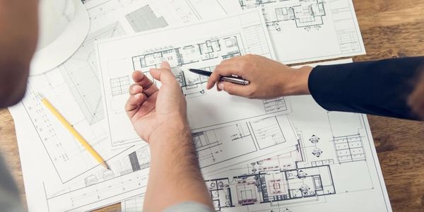 Two people discussing architectural blueprints on a wooden table.